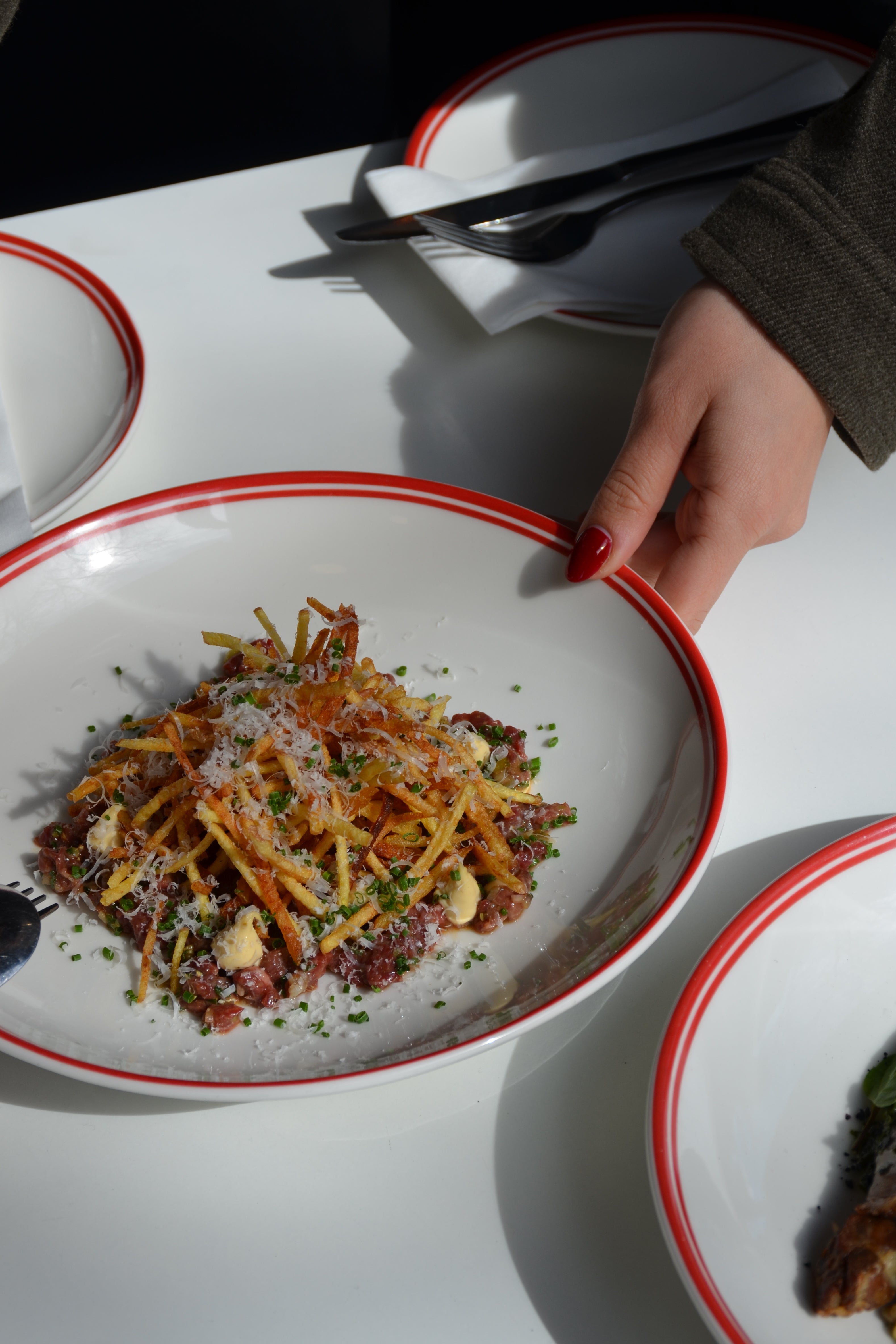 Hand holding a plate with a dish of food on a white table.